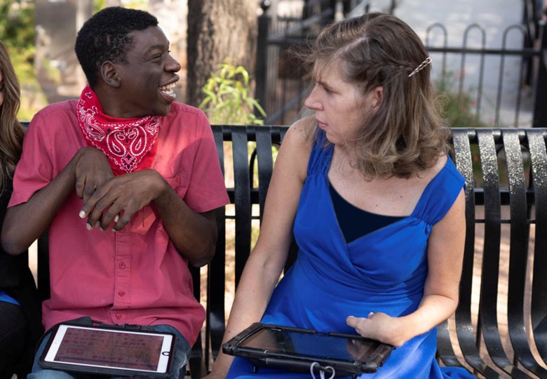 Boy and girl sitting on bench using their speech generating devices