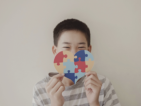 child holding up heart with puzzle shapes on it