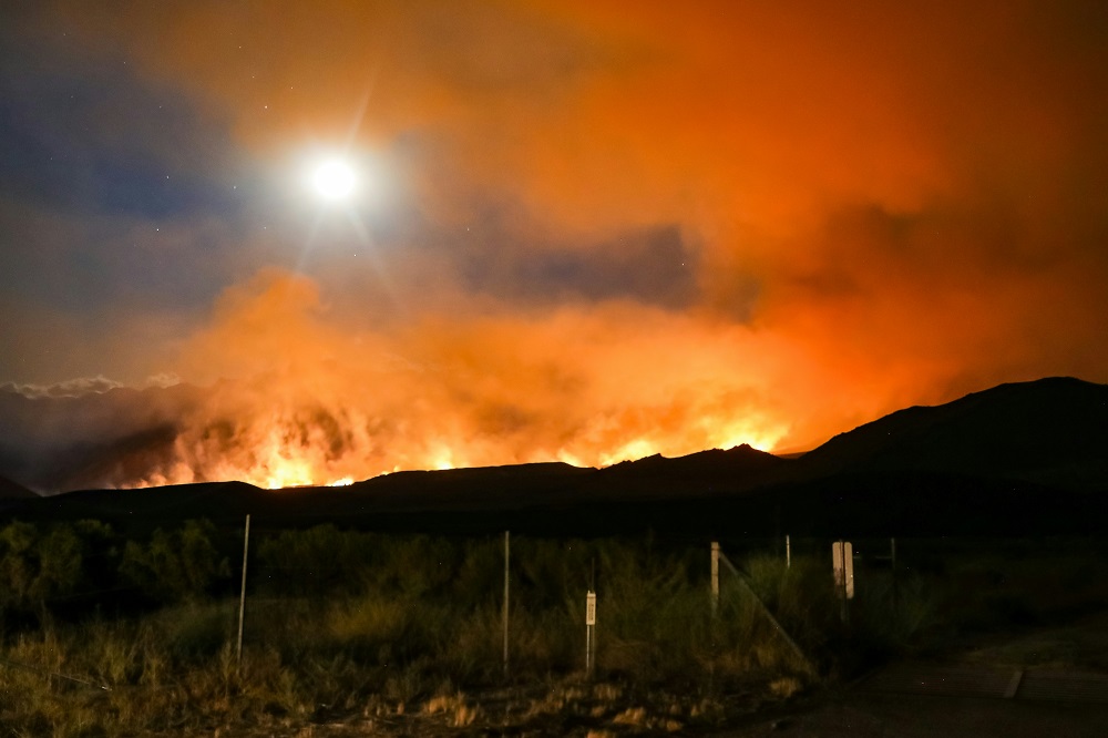 green grass field under blue sky during daytime with flames and smoke in the distance