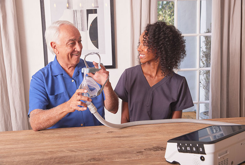 Non Invasive Vent NHV BlackFemaleClinicianWhiteMale SittingAtDiningTable Ventilator Luisa2 web flip