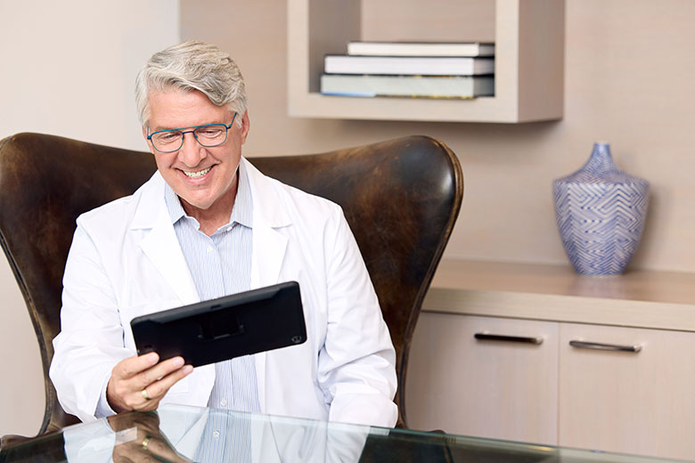 Telehealth WhiteMaleDoctorwithGlassesSmiling TalkingonTablet web flip