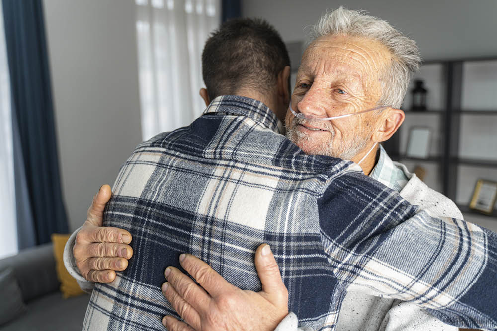 embrace of younger man and older man with tubes in nose