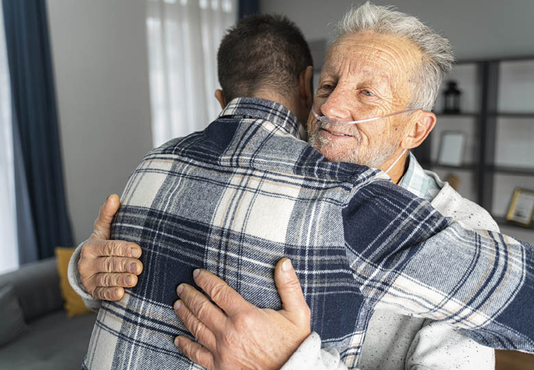 embrace of younger man and older man with tubes in nose