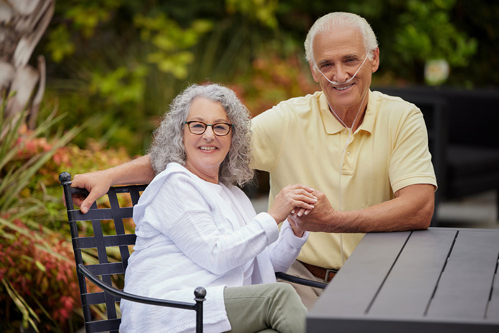 Oxygen White Couple Sitting at Table Outside Holding Hands Nasal Cannula2