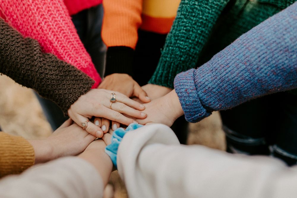 group of people in sweaters with their hands stacked together 