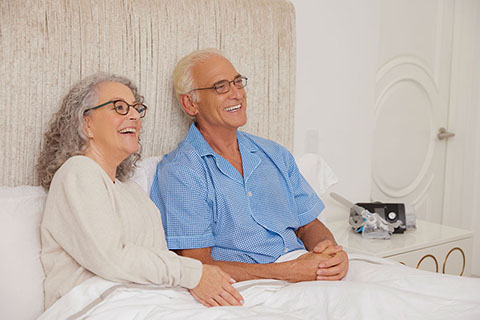 Sleep Apnea WhiteOlderCouple Smiling SittingUpInBed Lifestyle ResMedAirSense10 PAPMask