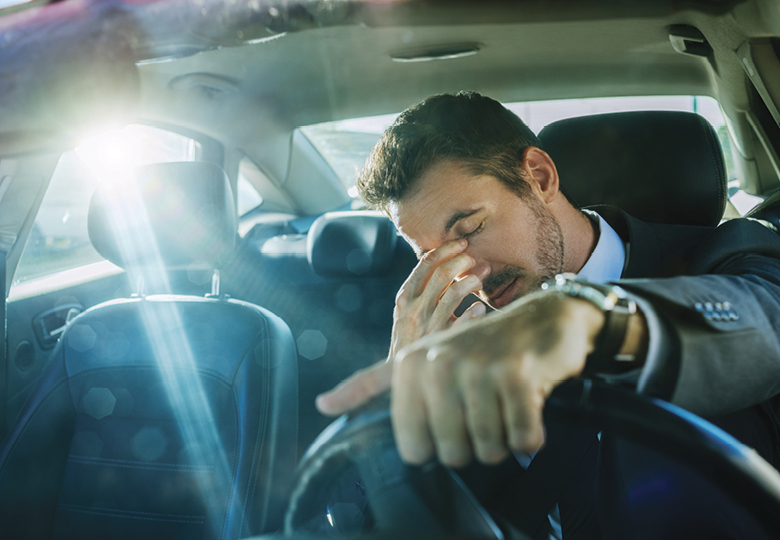 A man rubbing his eyes in the driver's seat of a car