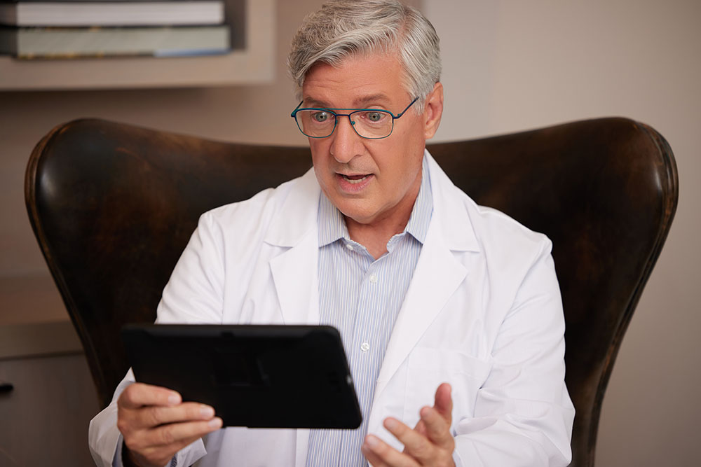 Telehealth White Male Doctor with Glasses Close Up Talking on Tablet