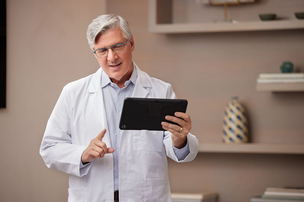Telehealth White Male Doctor with Glasses Standing Up Talking on Tablet Horizontal
